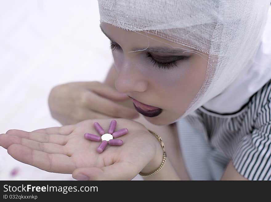 A beautiful girl with a bandage on a head holds pills on a palm. A beautiful girl with a bandage on a head holds pills on a palm