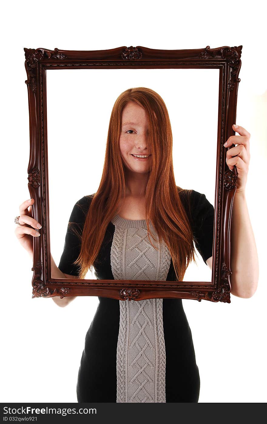 An young woman with long red hair holding a picture frame, in a black dress, with her hair over one eye, on white background. An young woman with long red hair holding a picture frame, in a black dress, with her hair over one eye, on white background.