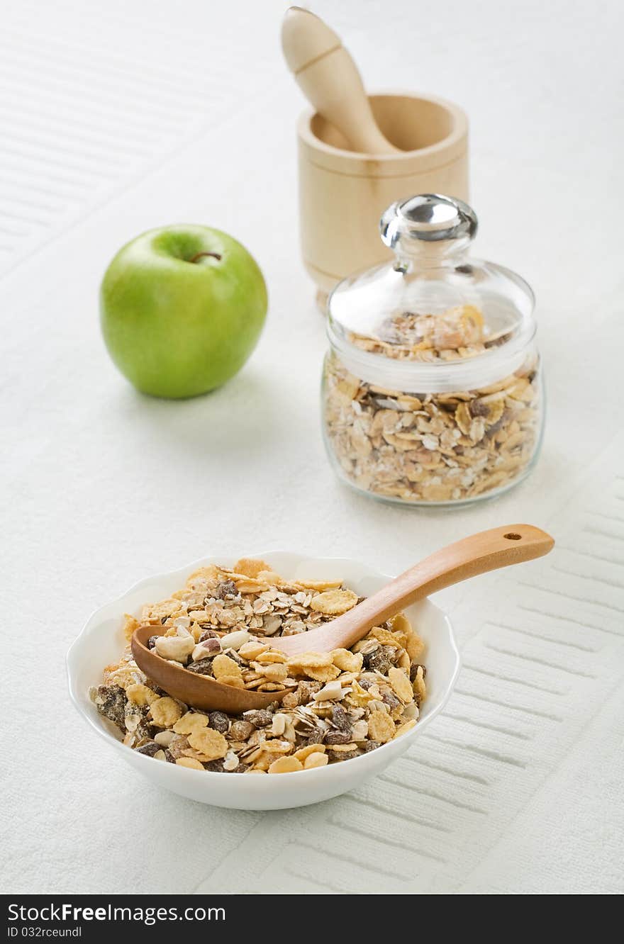 Composition of muesly in glass jar and white ceramic bowl and green apple and wooden mortar with pestle on white background. Composition of muesly in glass jar and white ceramic bowl and green apple and wooden mortar with pestle on white background