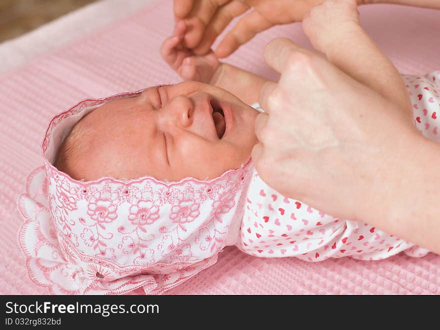 Mum swaddles the newborn girl in a pink cap. The girl cries. Mum swaddles the newborn girl in a pink cap. The girl cries