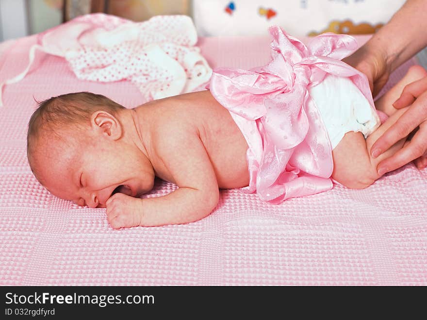 Mum swaddles the newborn girl in a pink cap. The girl cries. Mum swaddles the newborn girl in a pink cap. The girl cries