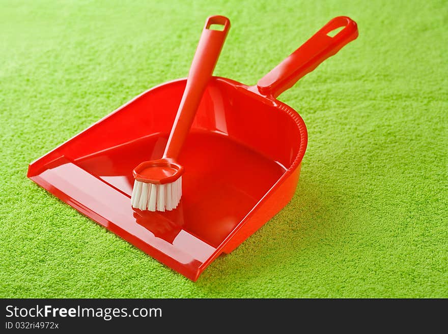 Red dustpan with brush on green cotton towel