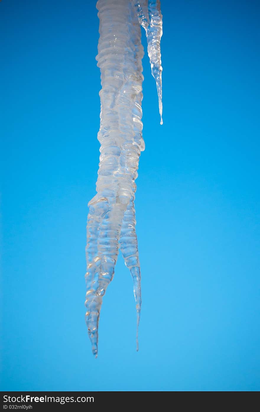 The sun shines through a large icicle with the blue sky in the background. The sun shines through a large icicle with the blue sky in the background.