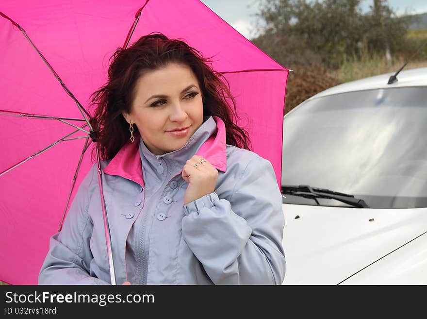 Beautiful lady with bright pink umbrella standing near her car. Beautiful lady with bright pink umbrella standing near her car