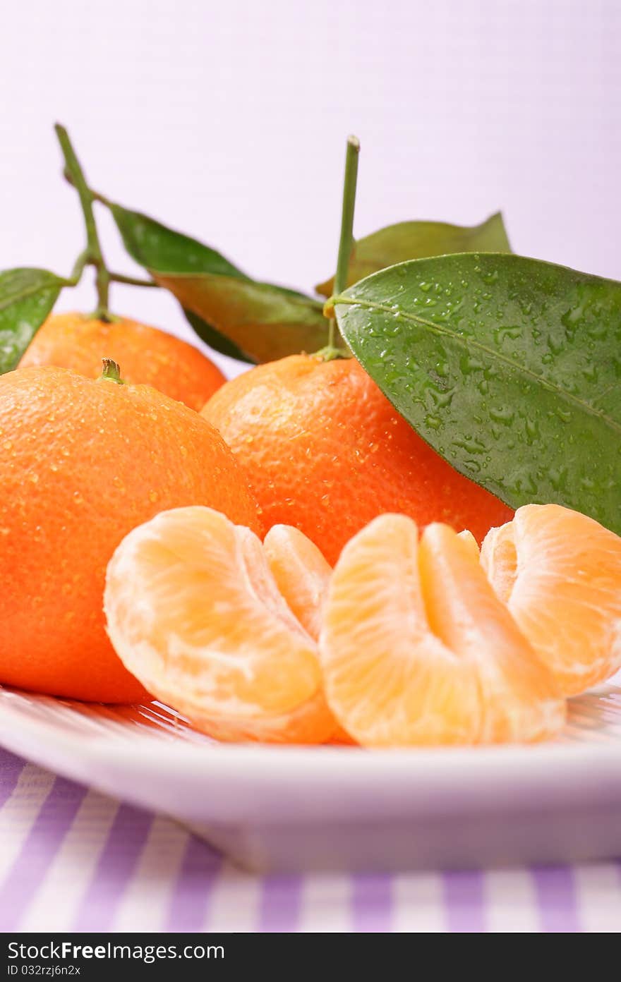 Whole and sectioned clementines served on a white dish. Studio shot. Selective focus, extra-shallow DOF.