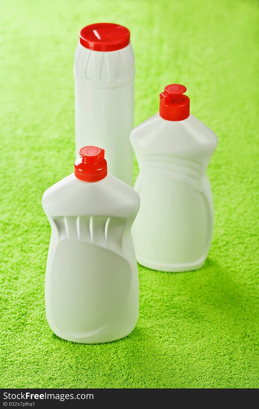 Three white plastical kitchen cleaners with red lids on green cotton towel. Three white plastical kitchen cleaners with red lids on green cotton towel