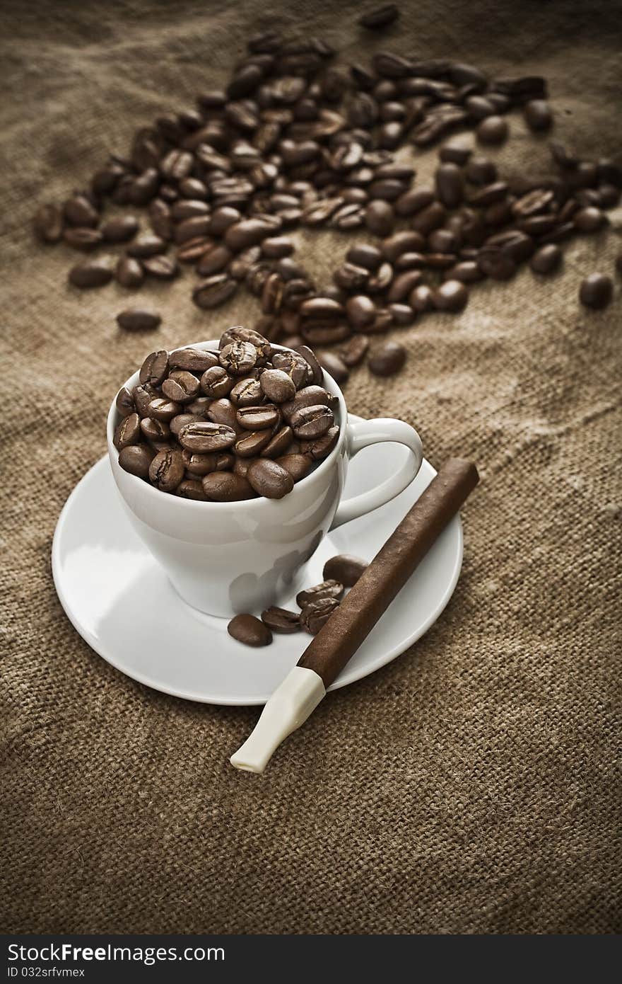 Cup with coffee beans and cigar on burlap