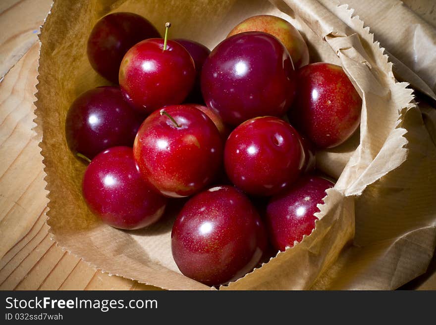 Organic red cherries and peach plum cherries in a brown paper bag on a wooden table. Organic red cherries and peach plum cherries in a brown paper bag on a wooden table