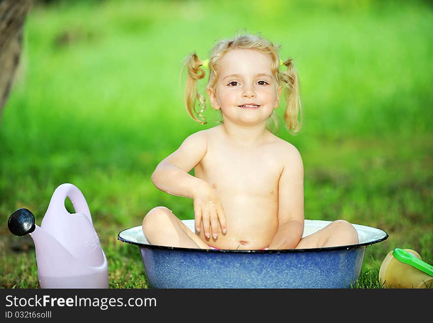 Little girl sits in basin with water. Hot summer day