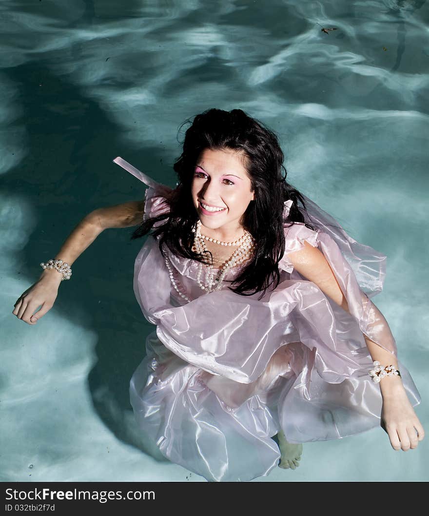 A woman in her fancy pink dress and pearl jewelry standing in water with a smile on her face. A woman in her fancy pink dress and pearl jewelry standing in water with a smile on her face.