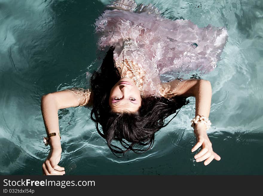 A woman laying on her back looking at the camera while she floats in the water in her pink dress. A woman laying on her back looking at the camera while she floats in the water in her pink dress.