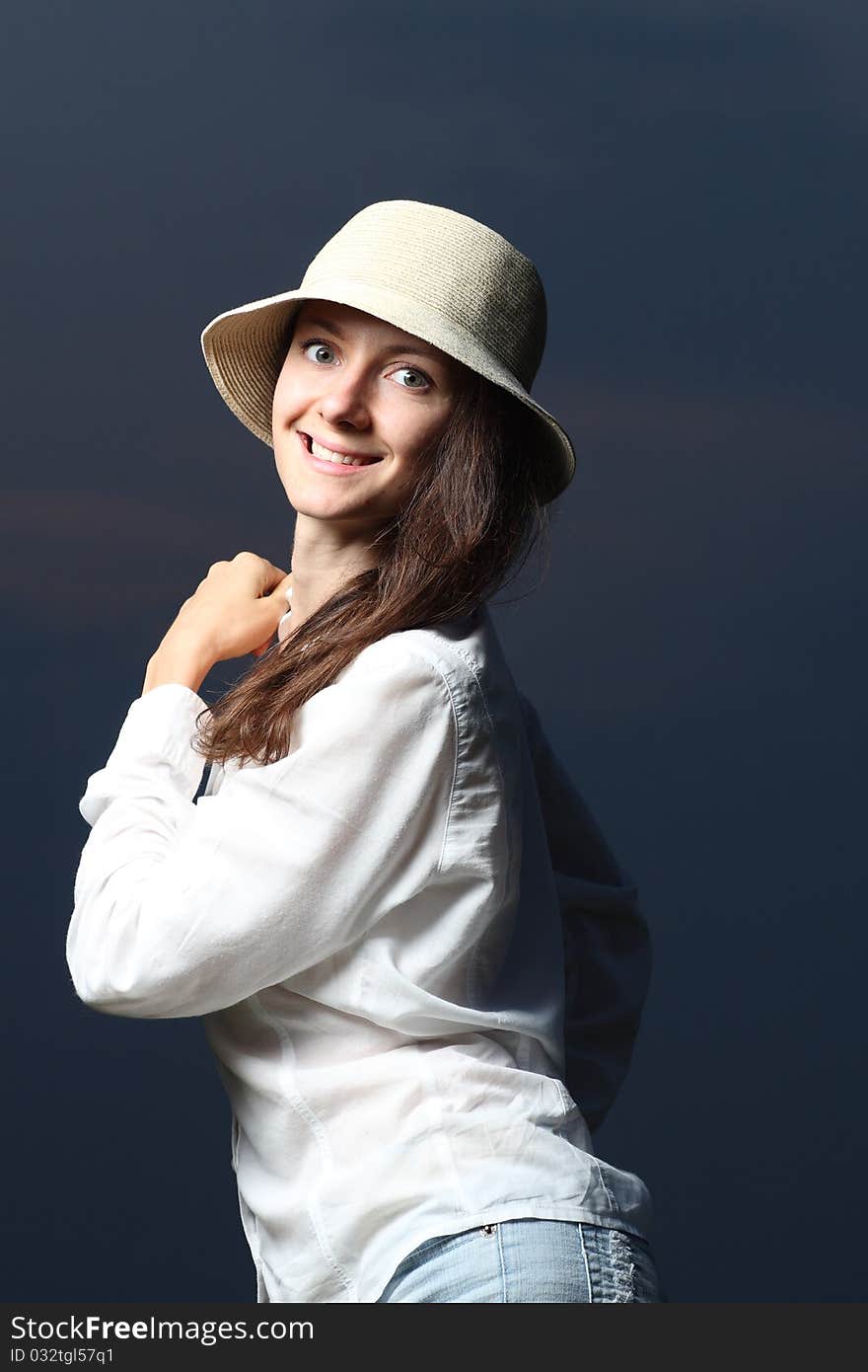 Portrait of a young smiling beautiful woman standing in darkness in a hat