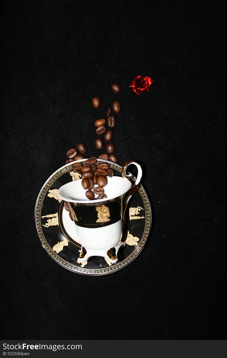 Abstract composition - Coffee beans are flying into the cup. A coffee cup on a black background, the coffee beans and one red crystal drop into the cup. Cup colors are white and black.