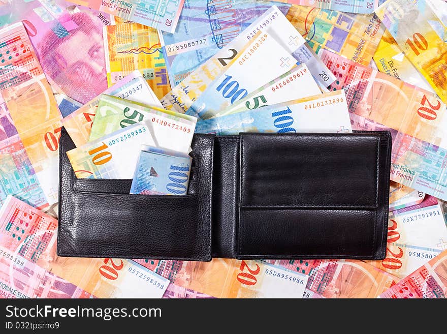 A black Wallet with Swiss Francs, is lying on a Table full of Swiss Francs. A black Wallet with Swiss Francs, is lying on a Table full of Swiss Francs