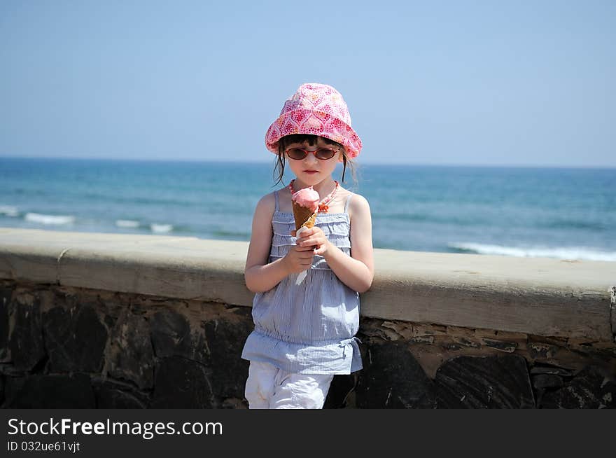 Small girl in glasses and sun hat on sea background with ice cream. Small girl in glasses and sun hat on sea background with ice cream