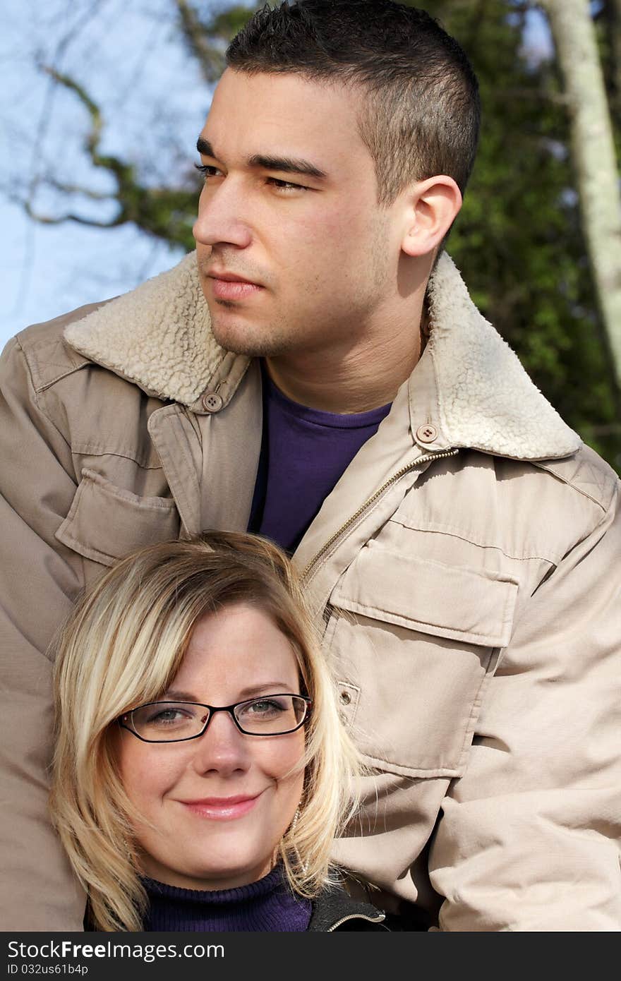 Autumn - outdoor shot of two young people as a close couple, satisfied looking. The man holds the woman standing behind her.