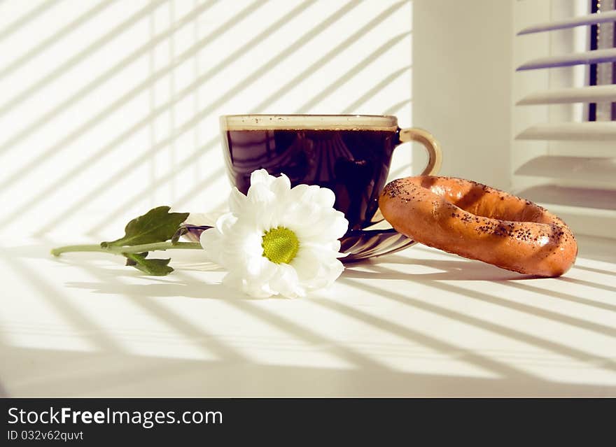 Mug of hot coffee and a flower on the windowsill