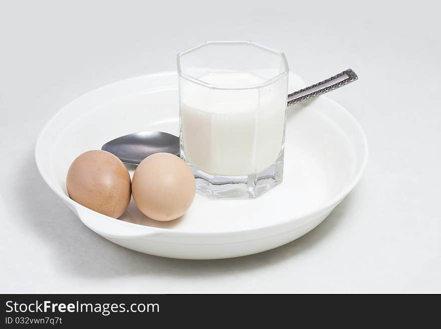 A glass of milk and two eggs in a white porcelain plate