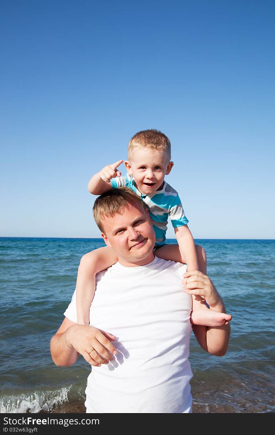 Father with son on shoulders on blue sky background on a beach. Father with son on shoulders on blue sky background on a beach