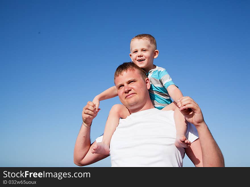 Father with son on shoulders on blue sky background on a beach. Father with son on shoulders on blue sky background on a beach