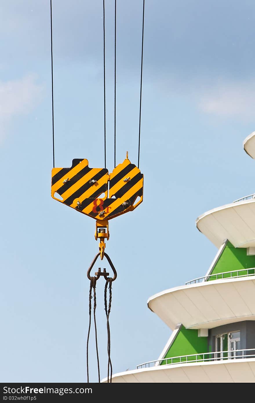 Crane hook and building fragment over blue sky with grey clouds