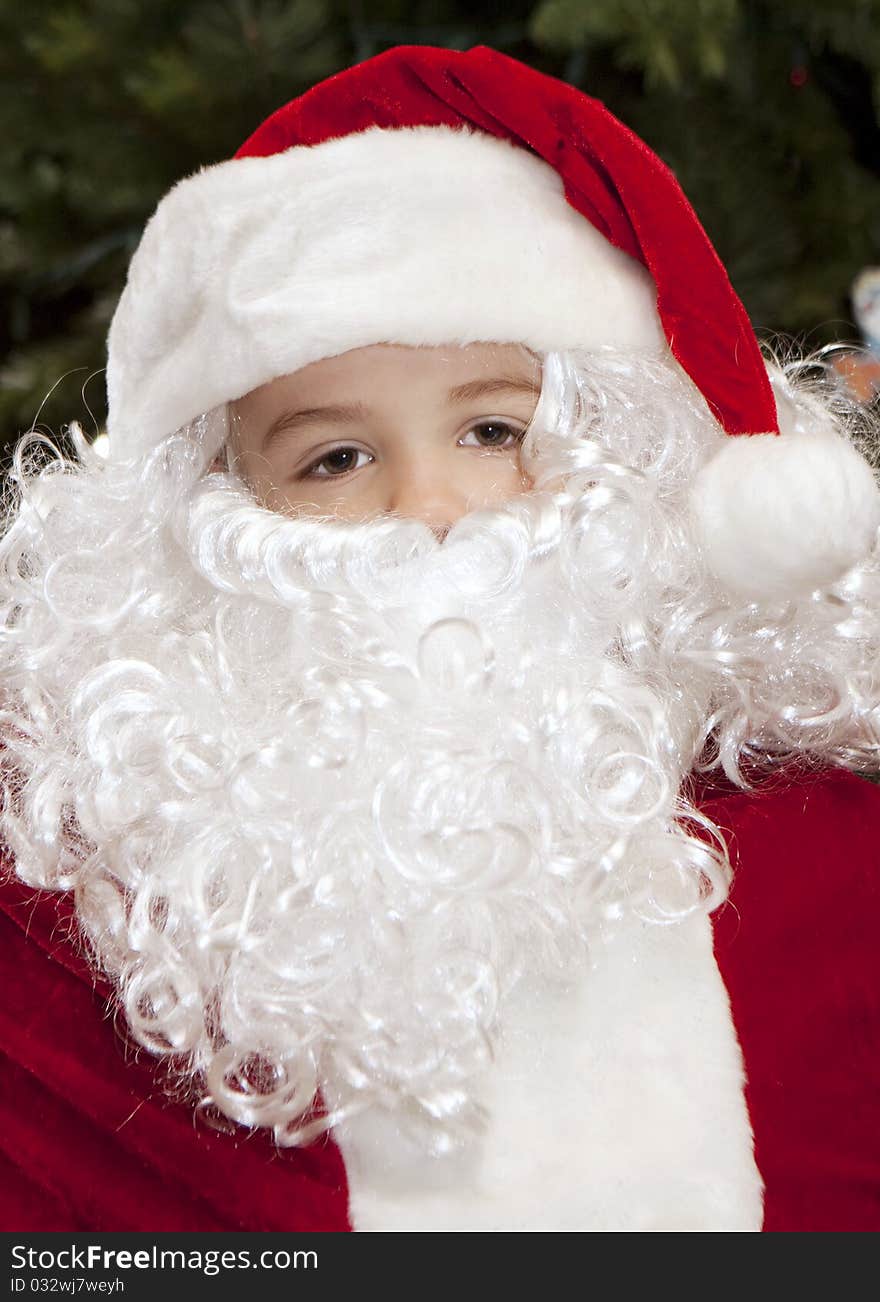 Thoughtful boy dressed as Santa Claus with a Christmas Tree backdrop.