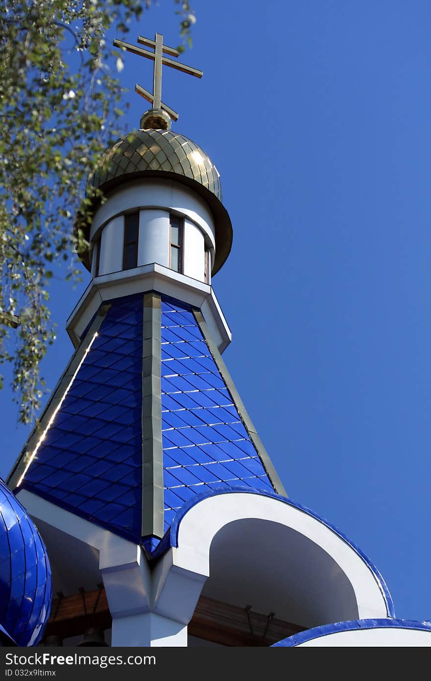 Dome with a cross of the Orthodox Church against the blue sky and the branches of birch. Dome with a cross of the Orthodox Church against the blue sky and the branches of birch