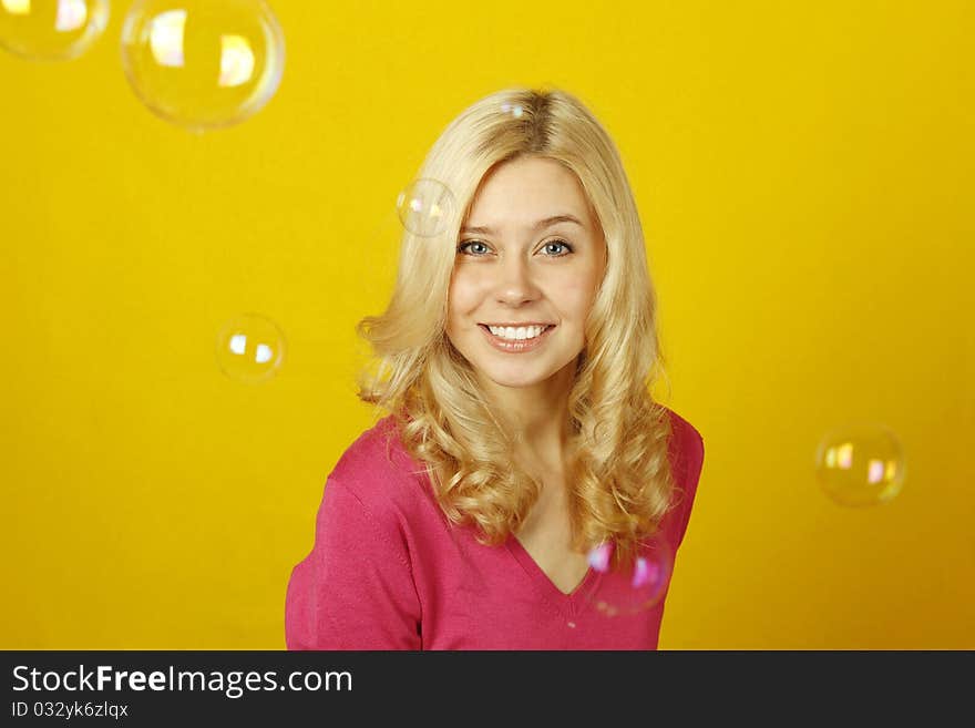 Young beautiful woman on a yellow background rejoices soap bubbles. Young beautiful woman on a yellow background rejoices soap bubbles