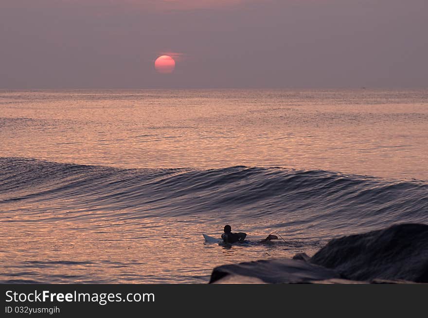 Silhouetted surfer catching wave at sunrise. Silhouetted surfer catching wave at sunrise