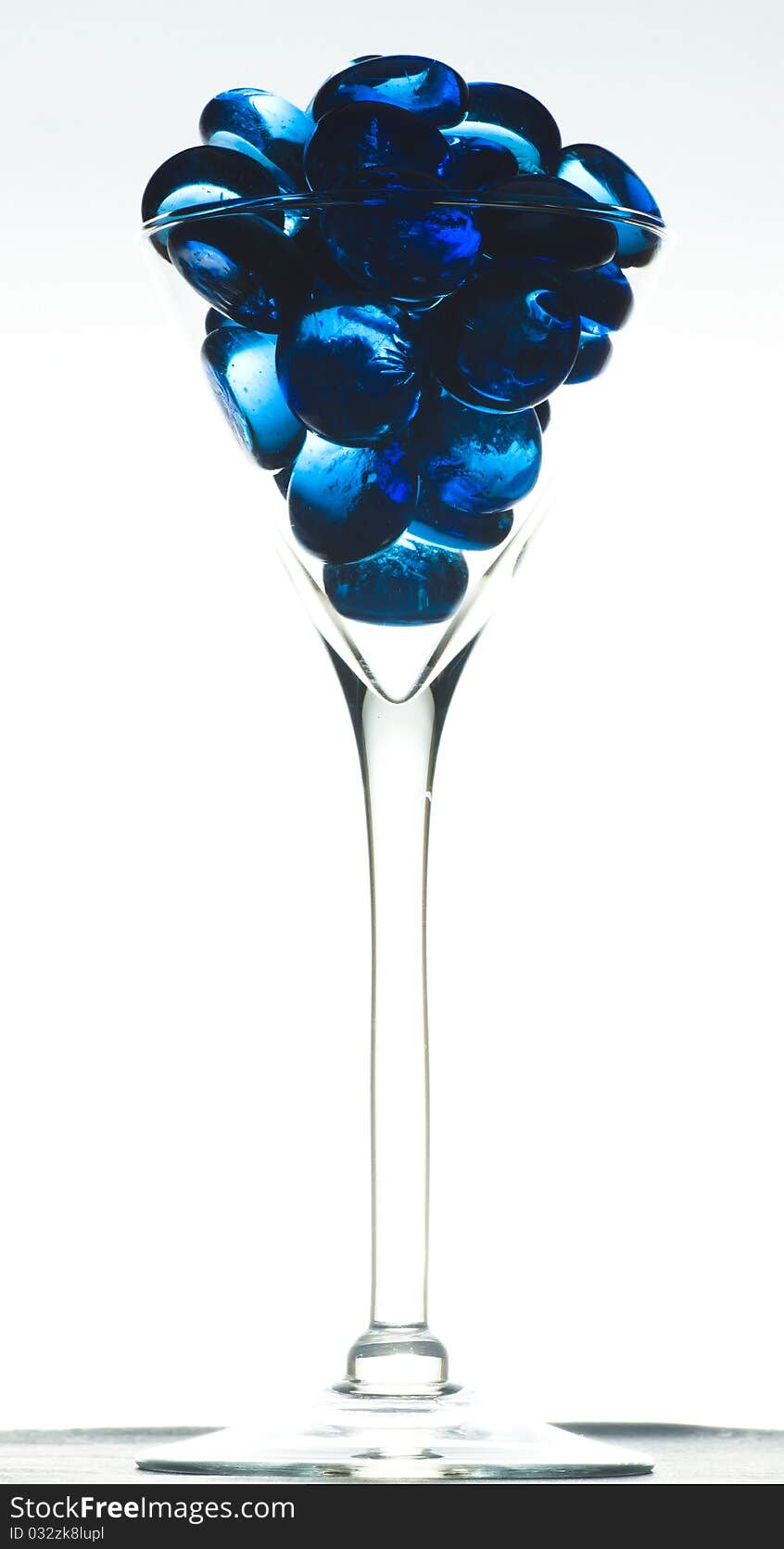 Isolated on white background part of  liqueur glass filled with blue glass small stone. Isolated on white background part of  liqueur glass filled with blue glass small stone