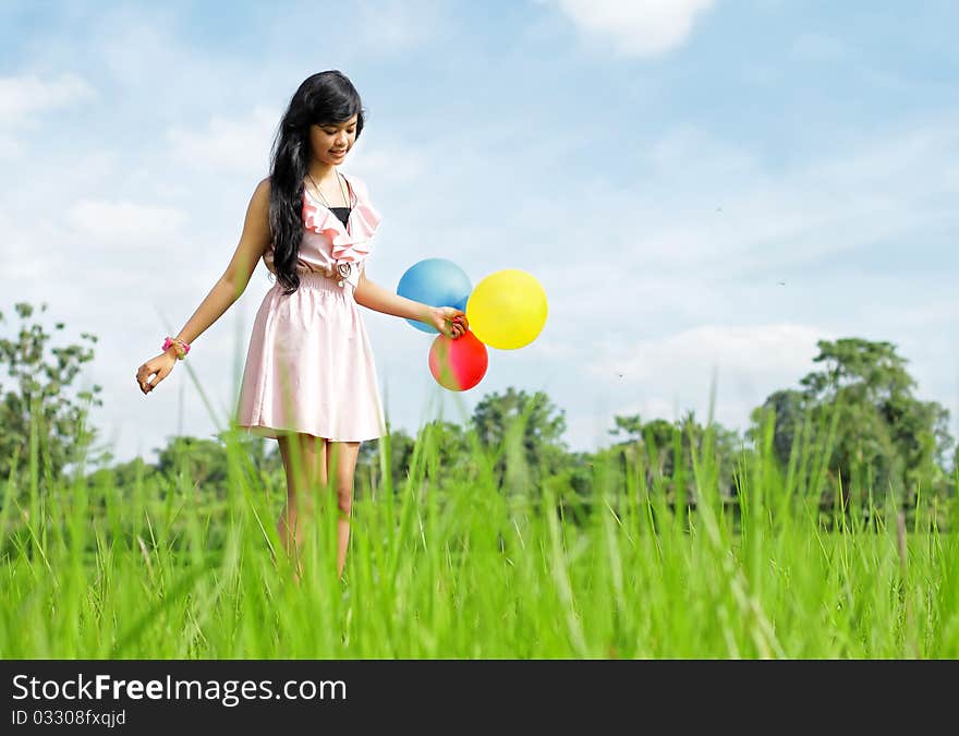 Young girl with colorful balloons stepping carefully in green nature