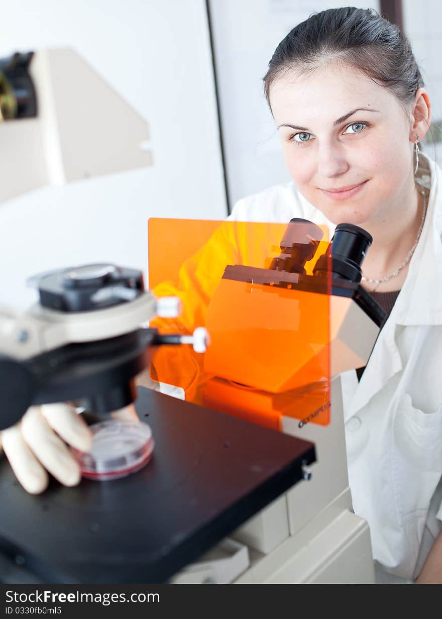 Pretty female researcher using a microscope in a lab