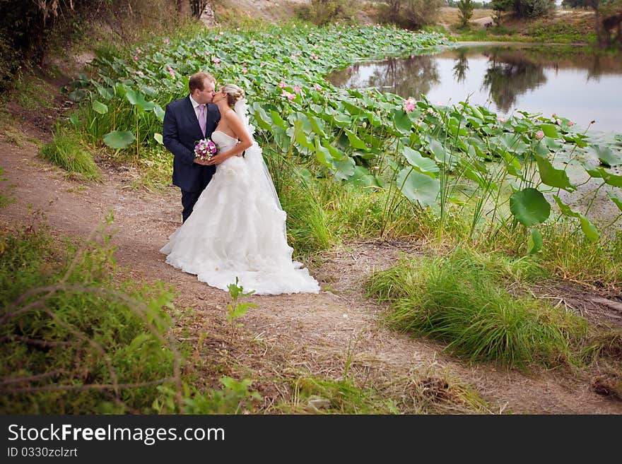 Kissing bride and groom near lotos pond