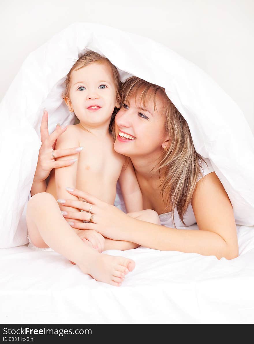 Young beautiful mother and her baby on the bed at home after the shower (focus on the baby)