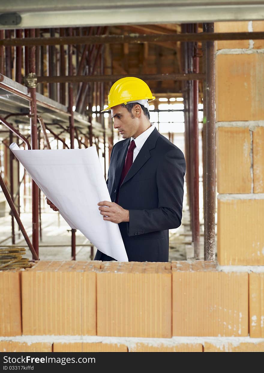 Caucasian male architect holding blueprints near brick wall. Vertical shape, waist up, side view, copy space. Caucasian male architect holding blueprints near brick wall. Vertical shape, waist up, side view, copy space