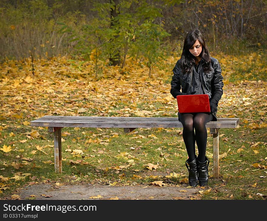 Beautiful young girl with red laptop in autumn park. Beautiful young girl with red laptop in autumn park