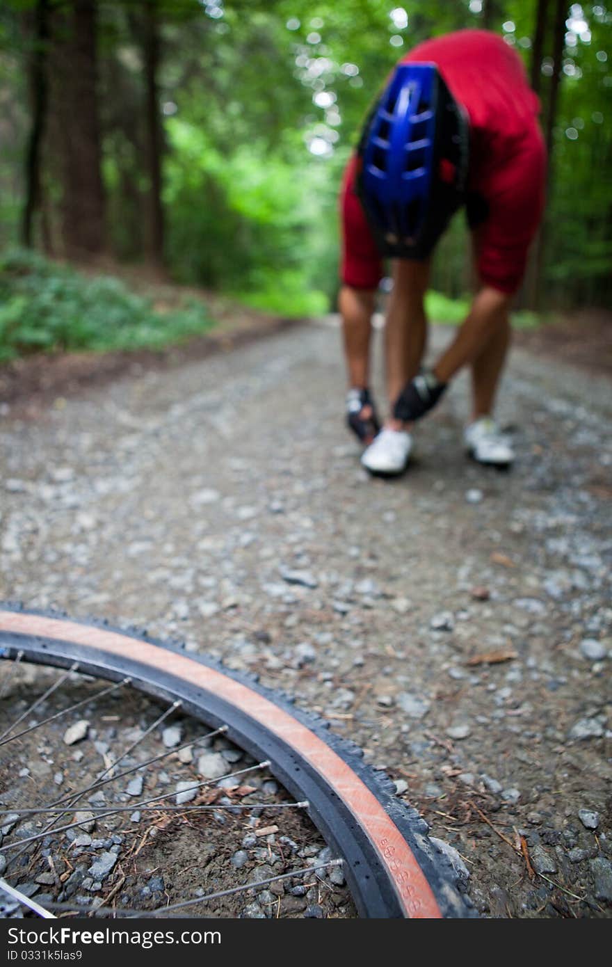 Mountain biking in a forest - bikers on a forest biking trail (shallow DOF, focus on the bike wheel in the foreground)