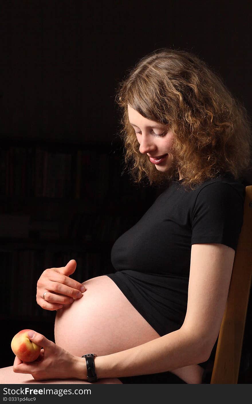 Smiling young pregnant woman with peach sitting on the chair. Smiling young pregnant woman with peach sitting on the chair