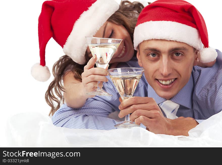 Young lovely couple in Santa hats holding the glasses of champagne and clinking glasses. Isolated over white background. (Focus is on champagne glasses). Young lovely couple in Santa hats holding the glasses of champagne and clinking glasses. Isolated over white background. (Focus is on champagne glasses)