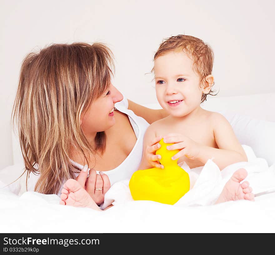 Young beautiful mother and her baby on the bed at home after the shower