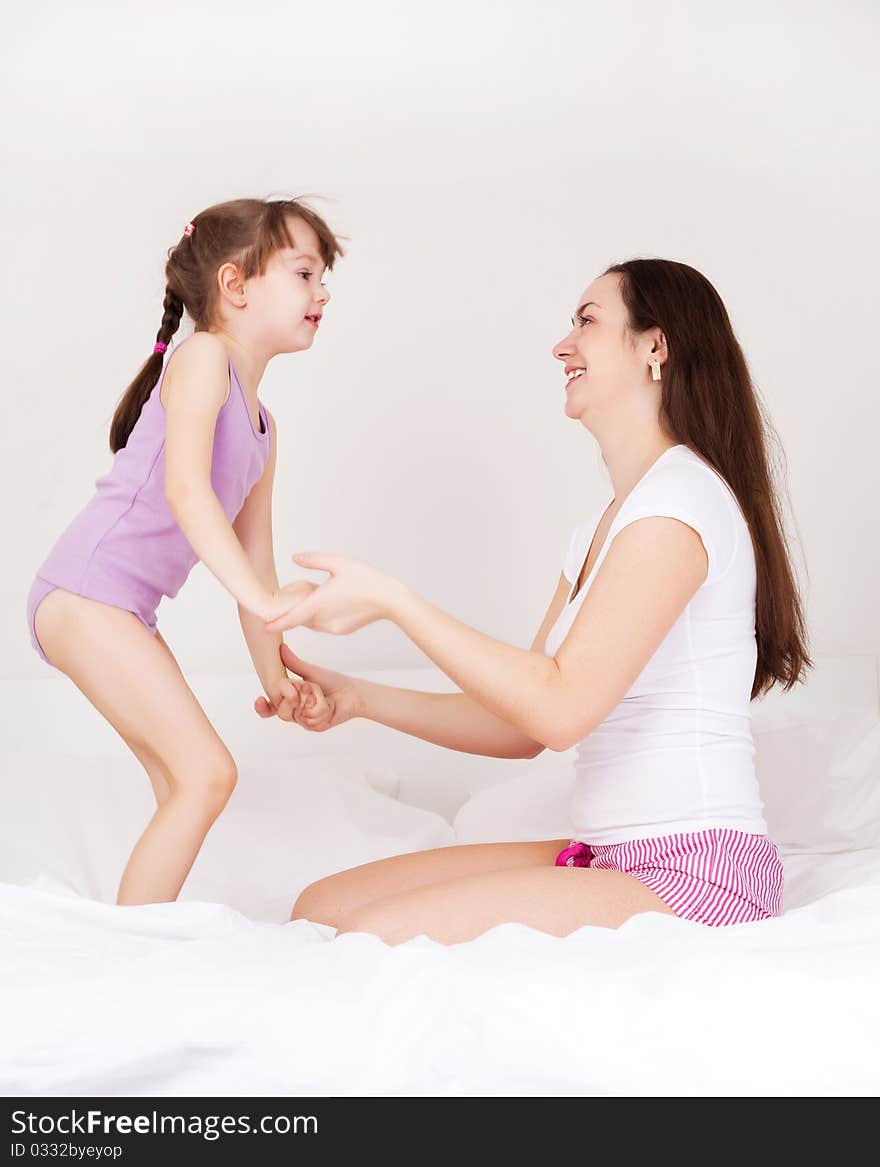 Beautiful young mother and her five year old daughter on the bed at home (focus on the mother). Beautiful young mother and her five year old daughter on the bed at home (focus on the mother)