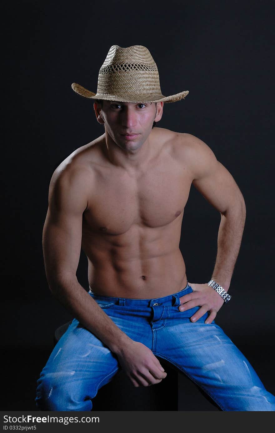 Sexy young male isolated against black wearing straw hat low key. Sexy young male isolated against black wearing straw hat low key