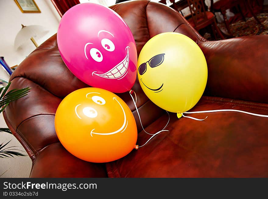 Three fanny red yellow and orange balloons on brown leather chair. Three fanny red yellow and orange balloons on brown leather chair