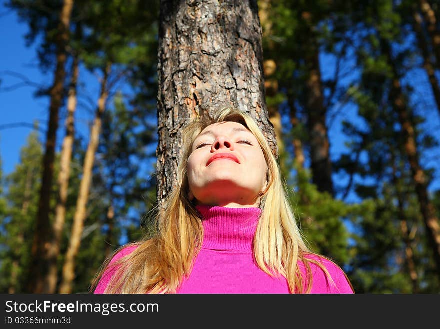 Beauty woman breathes near trunk of pine