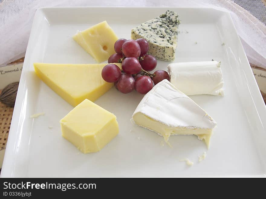 Assorted cheese on plate with a bunch of grape