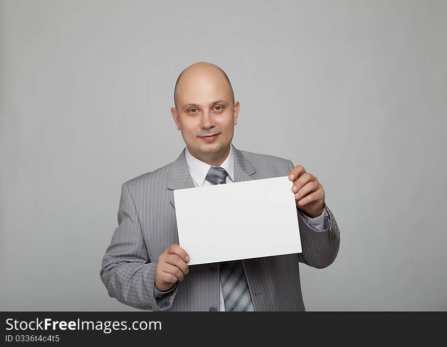 Bald businessman in a gray suit with a gray background with a white square in the hands of