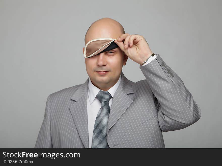 Bald businessman in a gray suit with a gray background with a bandage to sleep in his eyes