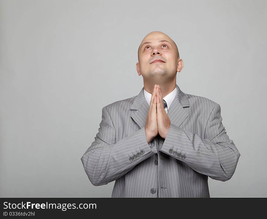 Bald businessman in a gray suit with a gray background makes various hand gestures