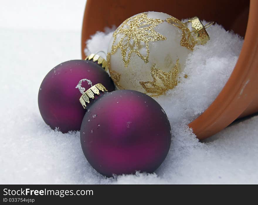 Christmas ornaments in a clay pot that is toppled over in the snowy garden. Christmas ornaments in a clay pot that is toppled over in the snowy garden.