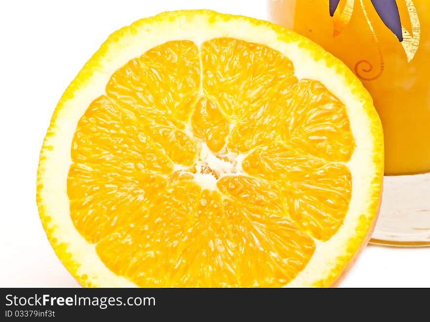 One big orange near a small glass with juice